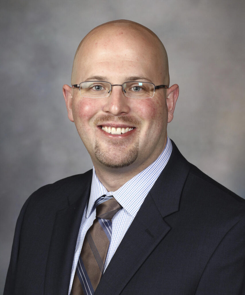 Headshot of man with glasses in jacket and tie